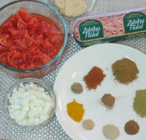 The ingredients for keema - ground chicken meat, canned tomatoes and cut up onions in a bowl, as well as all the spices measured and put on a plate.