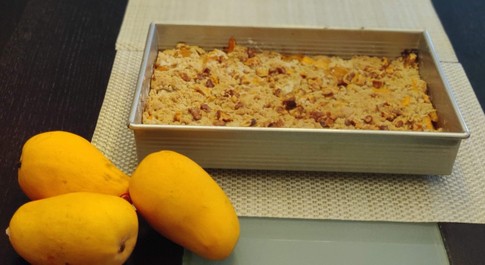 mango cobbler in a baking tray with fresh mangoes