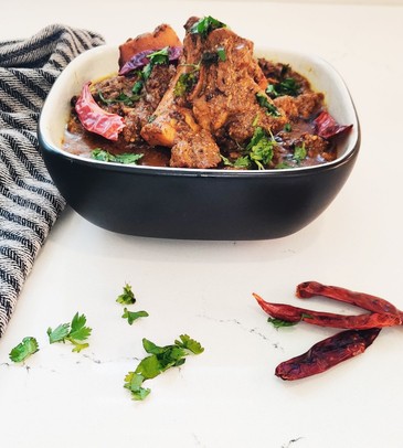 lamb curry in a serving bowl on a white counter beside a dish cloth and hot peppers