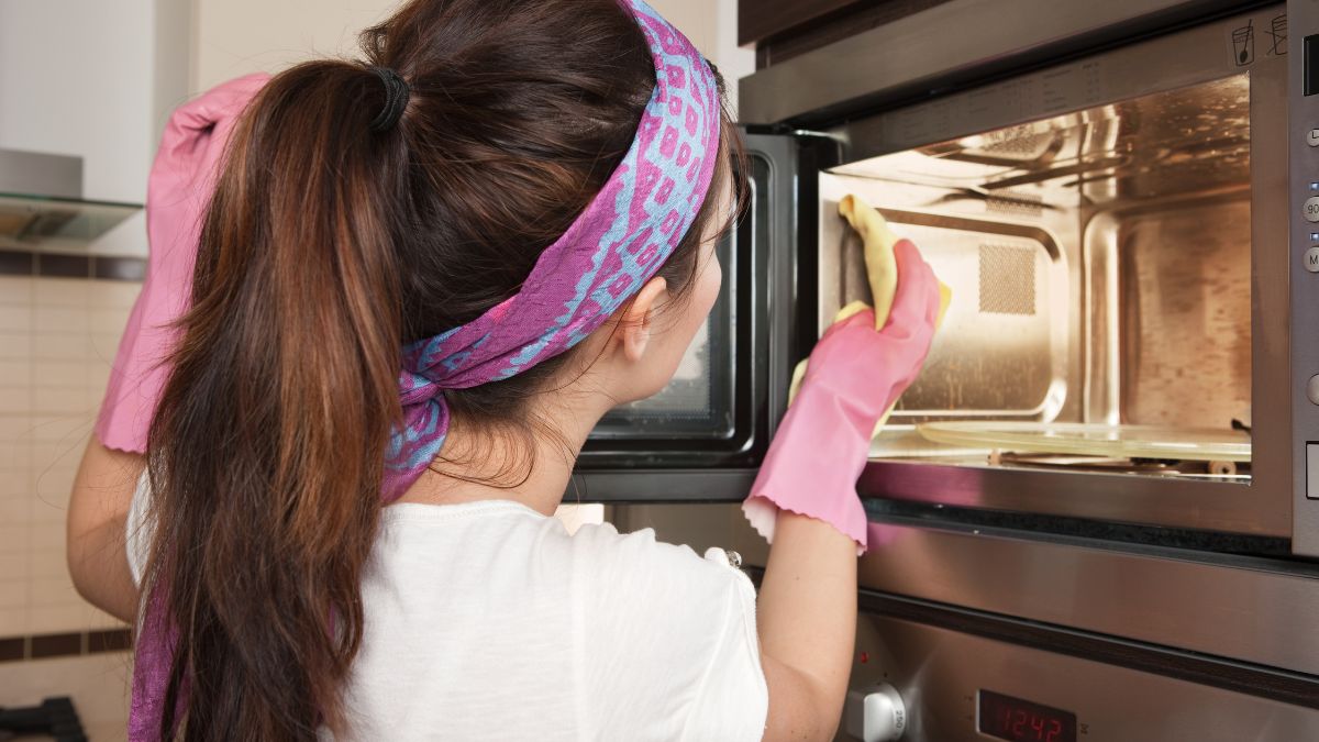 woman with pink rubber gloves on wiping down the inside of a microwave.