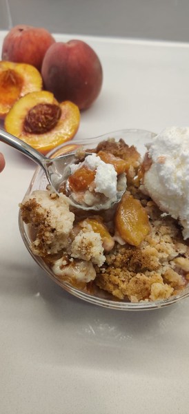 peach cobbler with cut peaches on the counter beside the bowl