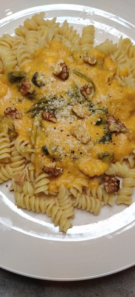 pumpkin spinach pasta on a plate garnished with toasted walnuts and parmesan cheese