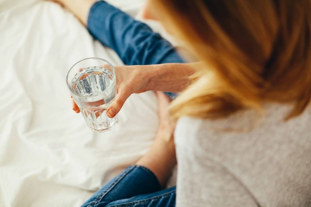 women holding glass of water while sitting on the bed