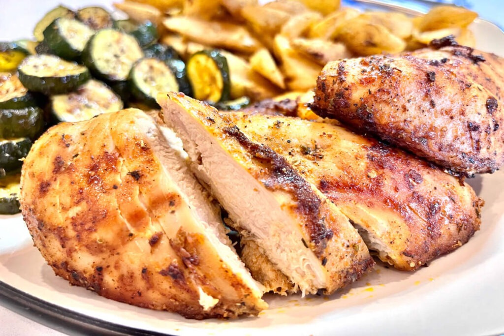 chicken breast with a side of zucchini slices and potato wedges.