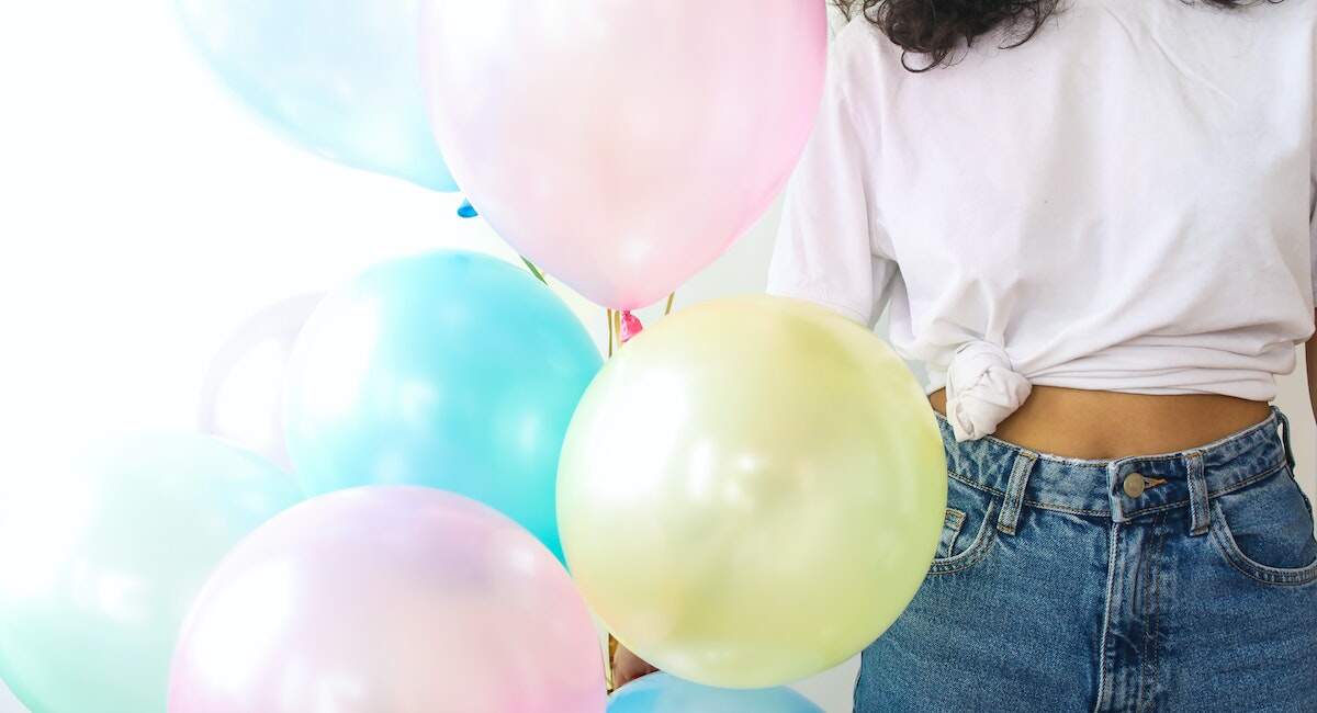girl wearing a t-shirt and jeans holding a big bouquet of balloons