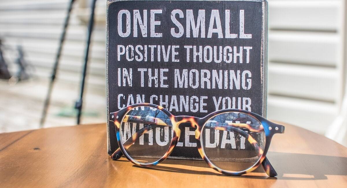 a quote on a board that says one small positive thought in the morning can change your whole day with a pair of glasses in front of it.