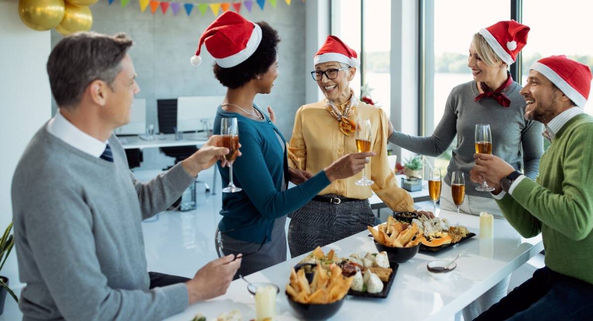 employees gathered to celebrate Christmas with santa hats on around food and drinks.