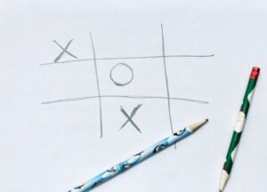 2 pencils and a game of tic tac toe on a piece of paper