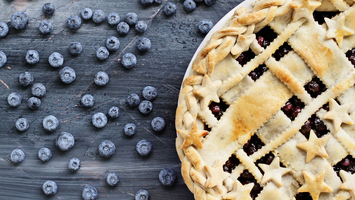 blueberry pie beside blueberries spread beside it.