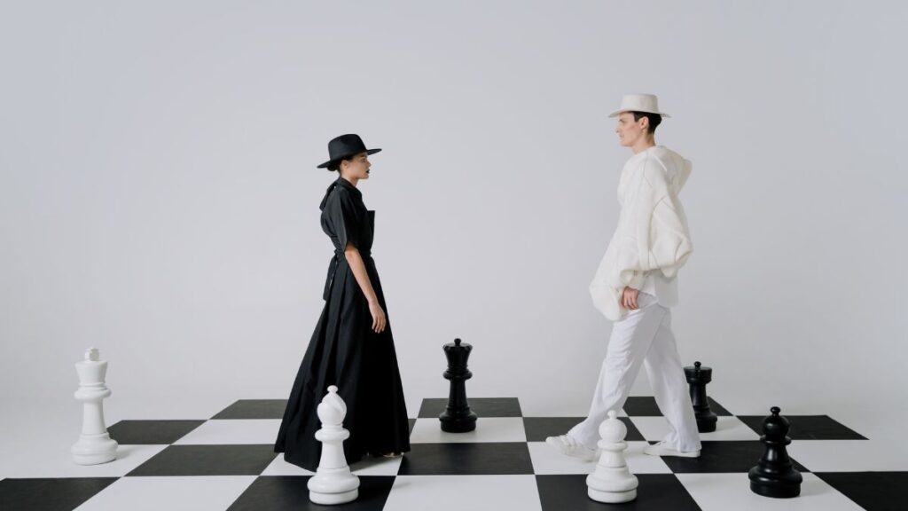 woman dressed in black and man dressed in white on a chess board.