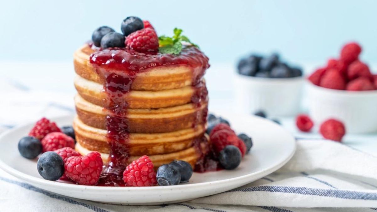 sheet pan pancakes stacked on a plate with syrup and berries.