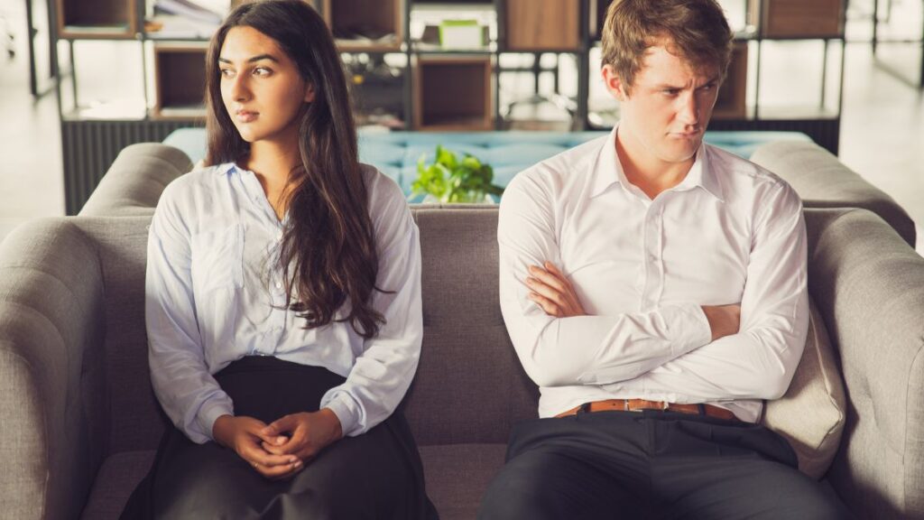 woman and man sitting apart on a couch looking upset.