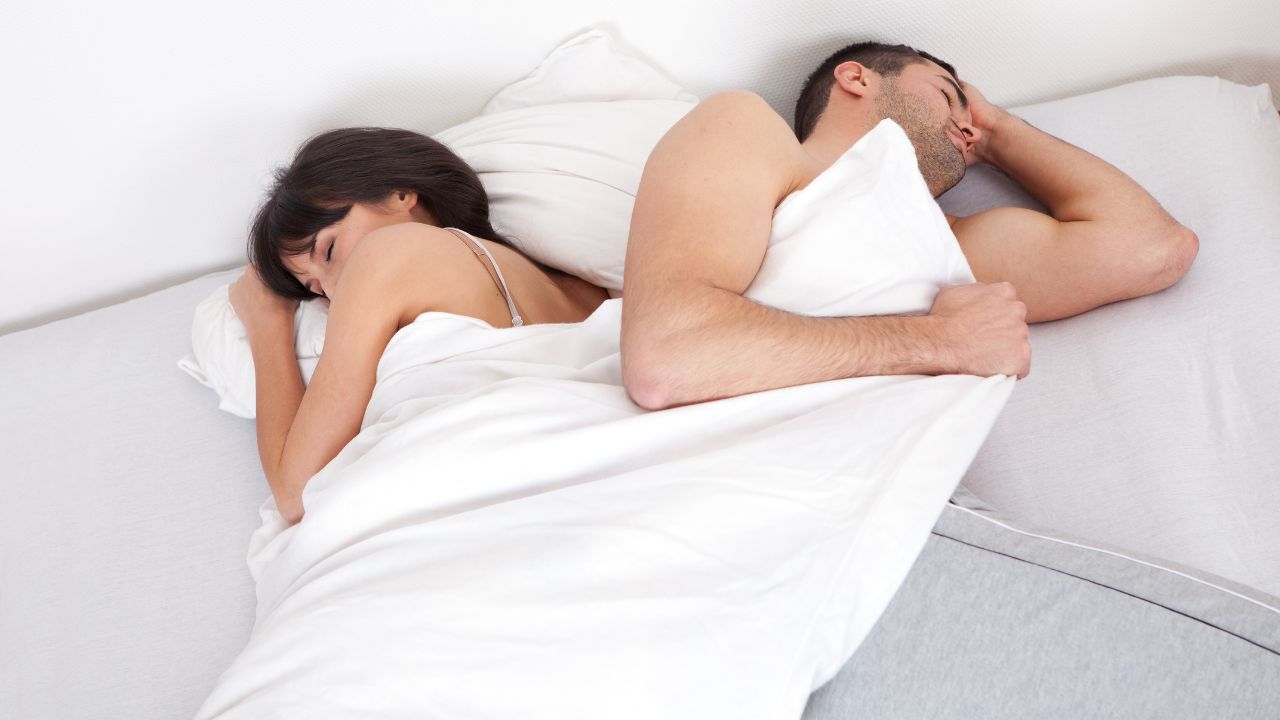 man pulling the blanket in bed with woman