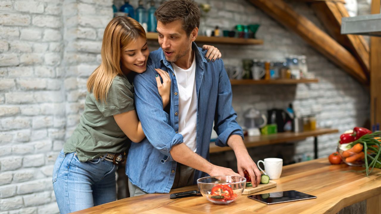woman hugging man from behind while he prepares a meal