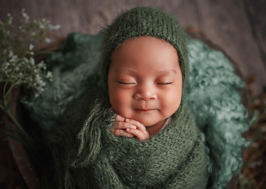 a baby swaddles in a green blanket.