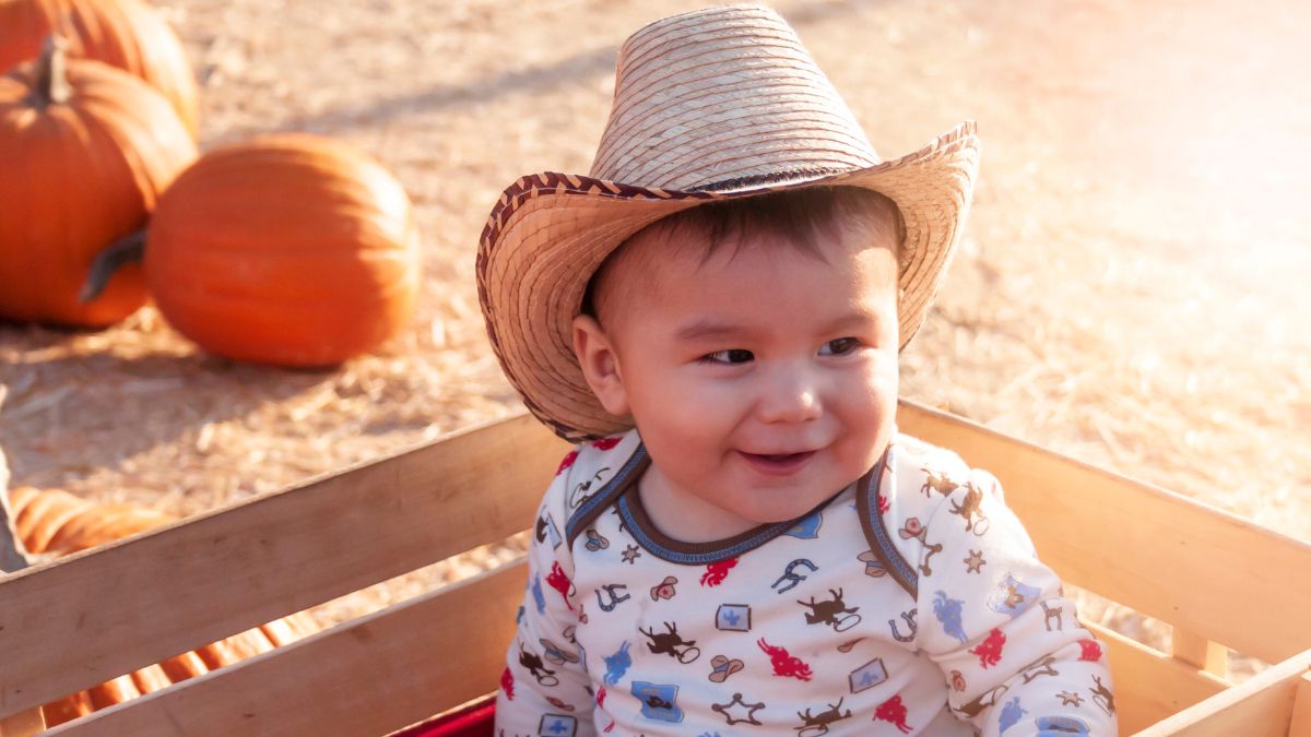 a baby boy with a western hat on in sitting in a wagon.