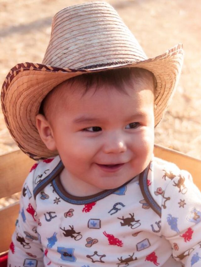 a baby boy with a western hat on in sitting in a wagon.