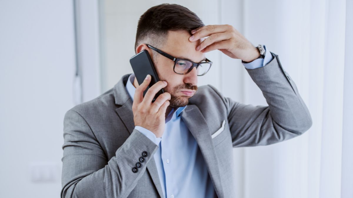 man with hand on head talking on cell phone looking stressed