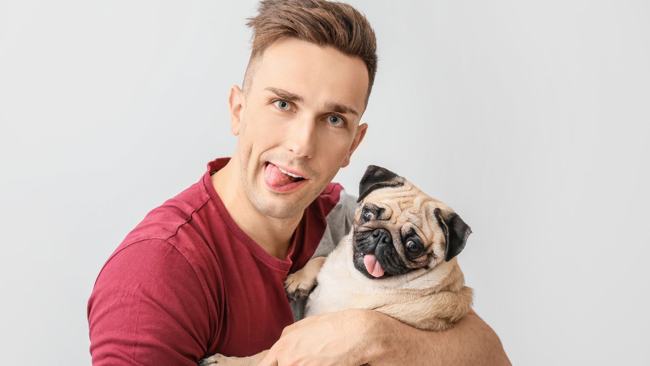 man holding pug and both are sticking their tongues out