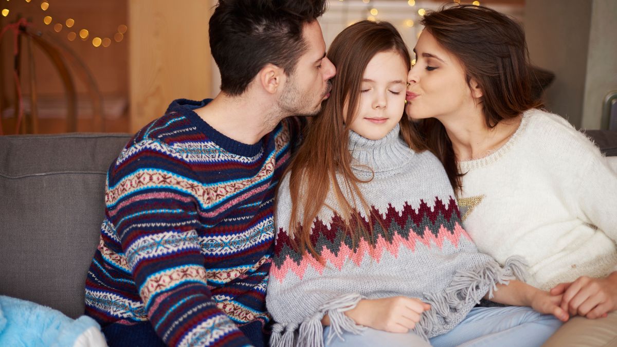 daughter sitting between mother and father as they kiss her