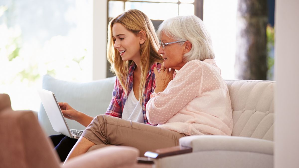older woman sitting on the sofa with a young girl looking at an open laptop.