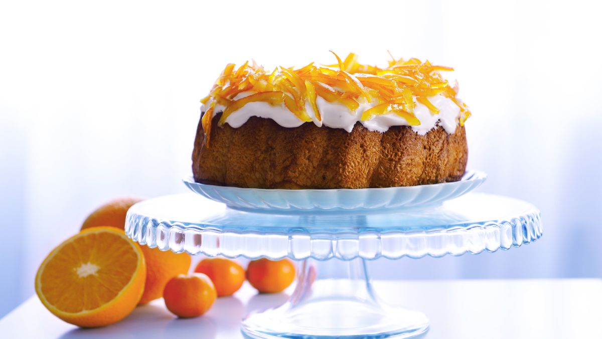 orange bundt cake with orange zest on top and orange halves beside the cake tray.