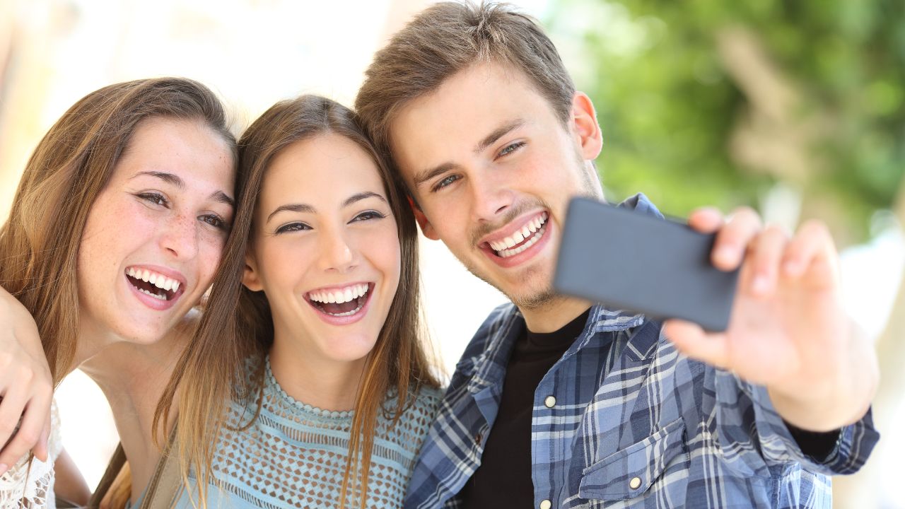 two women and a man smiling and standing together while the man takes a selfie of everyone