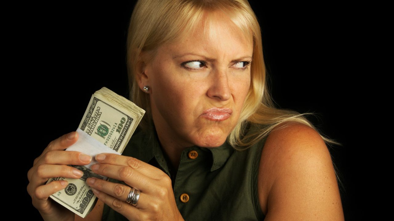woman holding on to money, making a scowling face