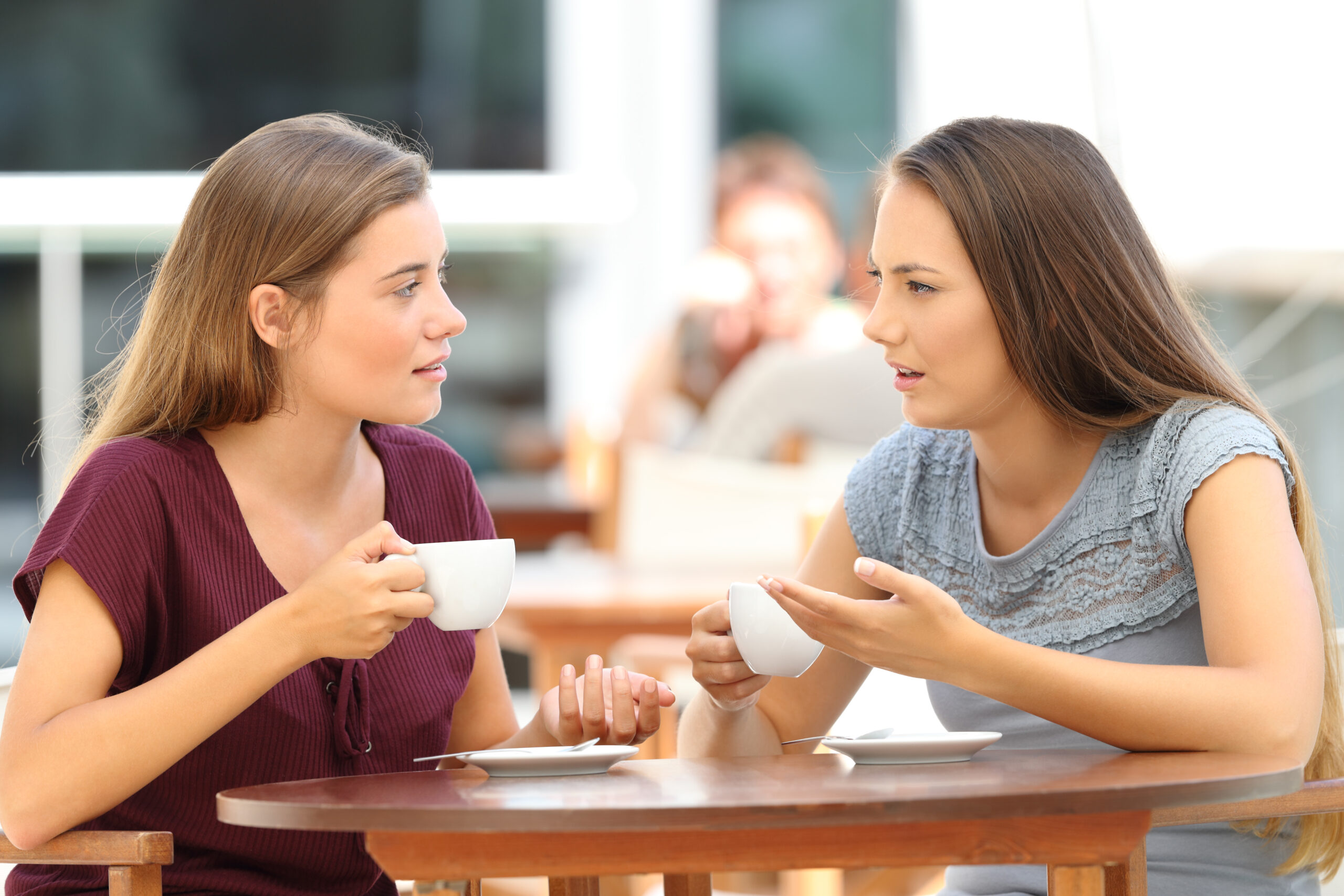 Two serious friends talking sitting in a restaurant drinking from tea cups
