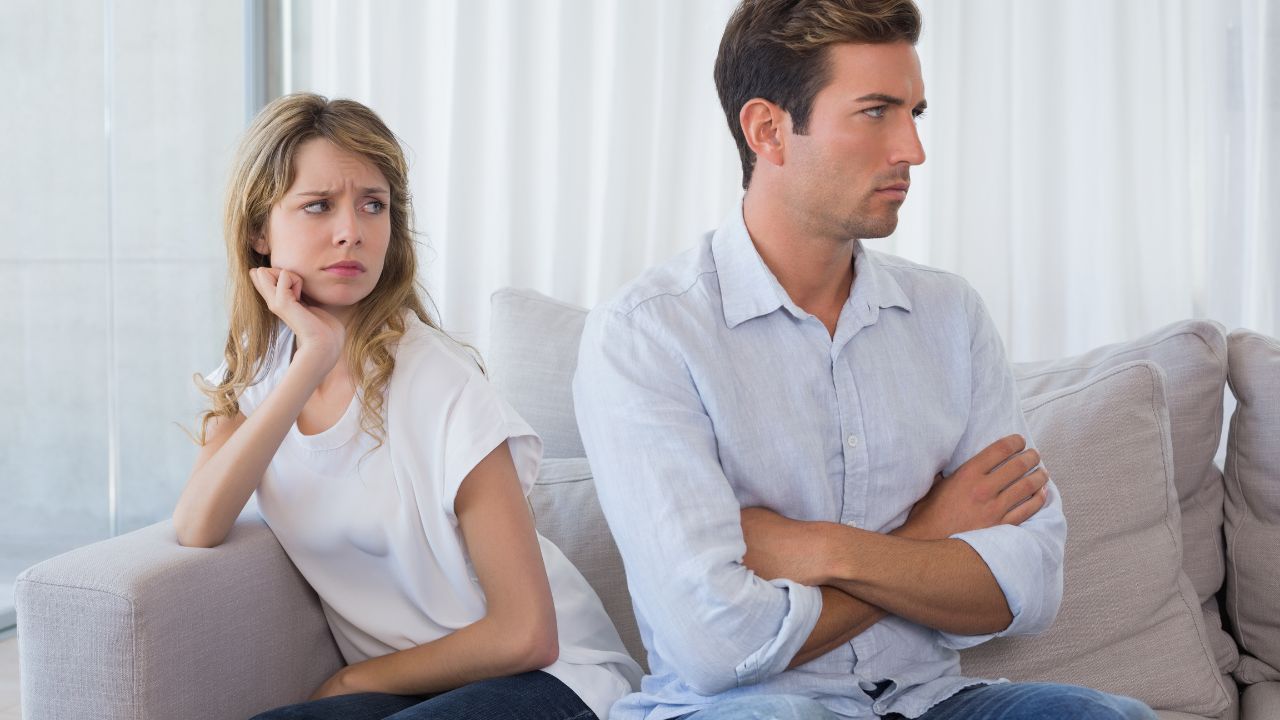 man has his back turned and arms crossed in anger as woman looks at him.