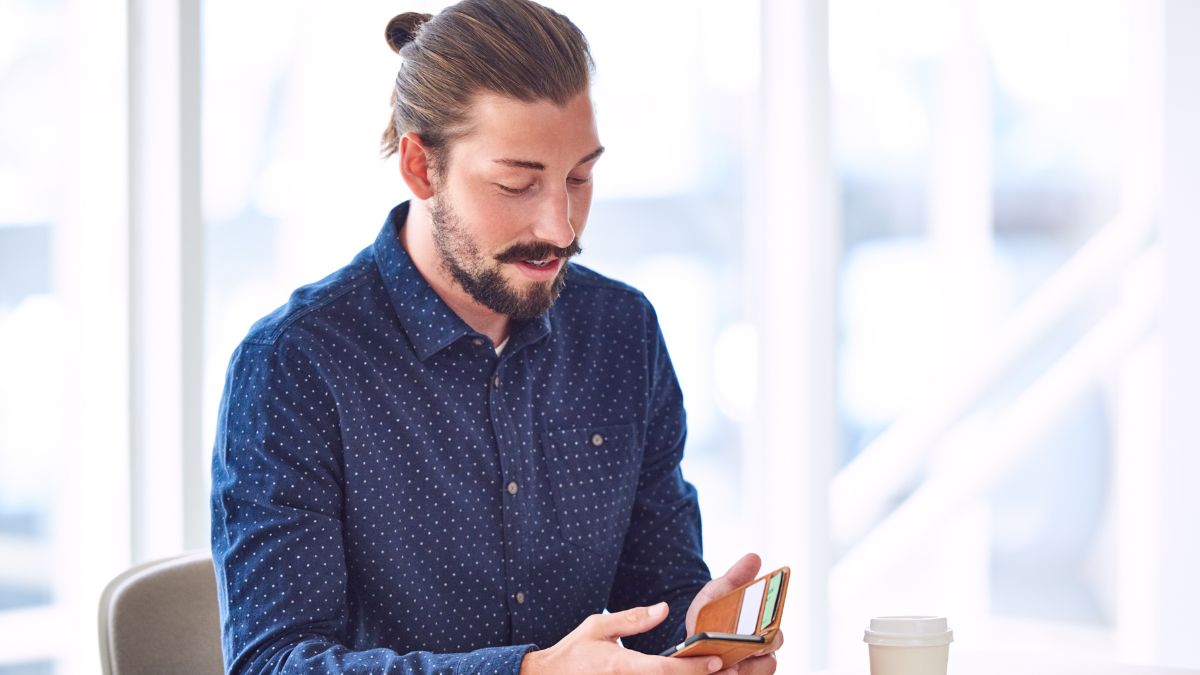 man with bun looking at phone and drinking coffee
