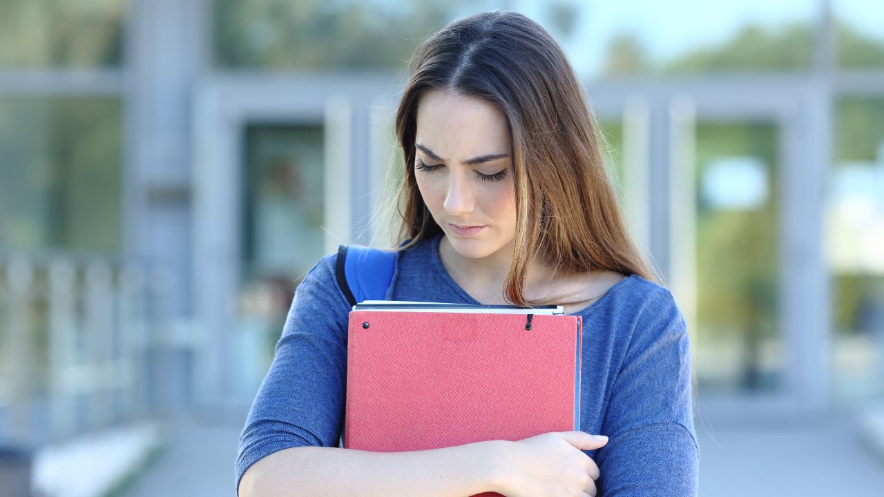 college girl looking down and looking sad while holding notebooks