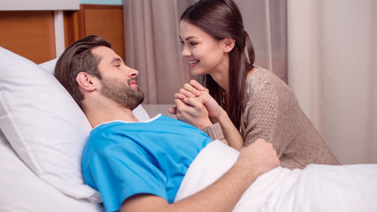 husband sick in hospital bed while wife holds his hand