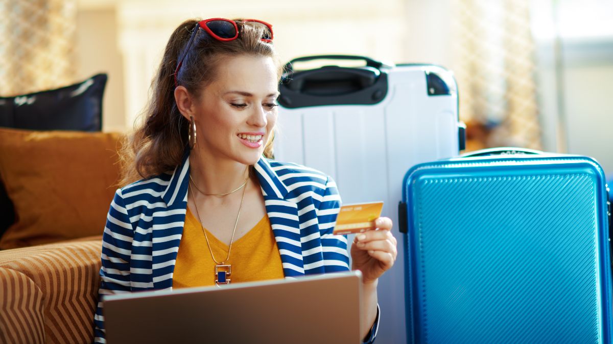 woman on a laptop holding her credit card sitting beside luggage.