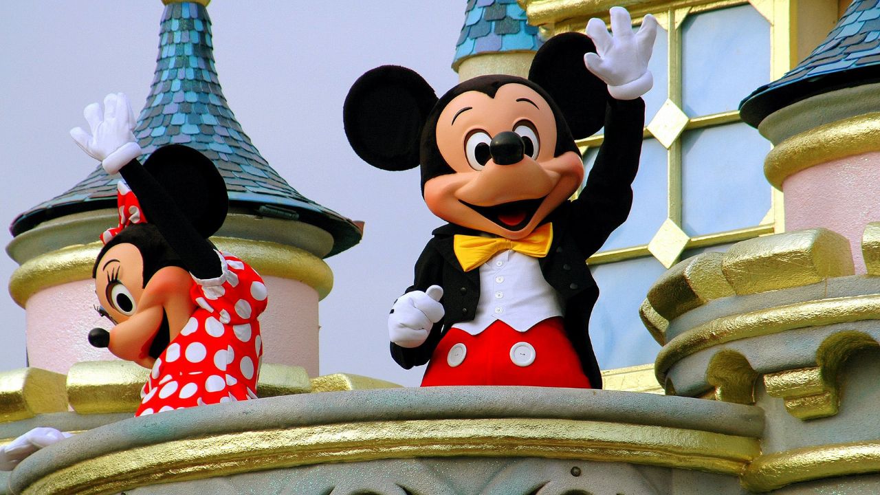 Mickey and Minnie Mouse waving from a Disney tower