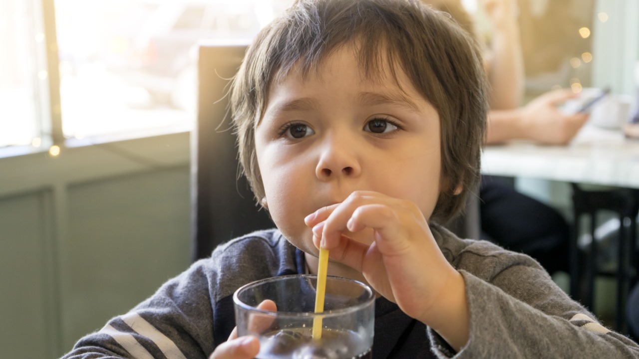 a boy drinking soda from a glass with a straw