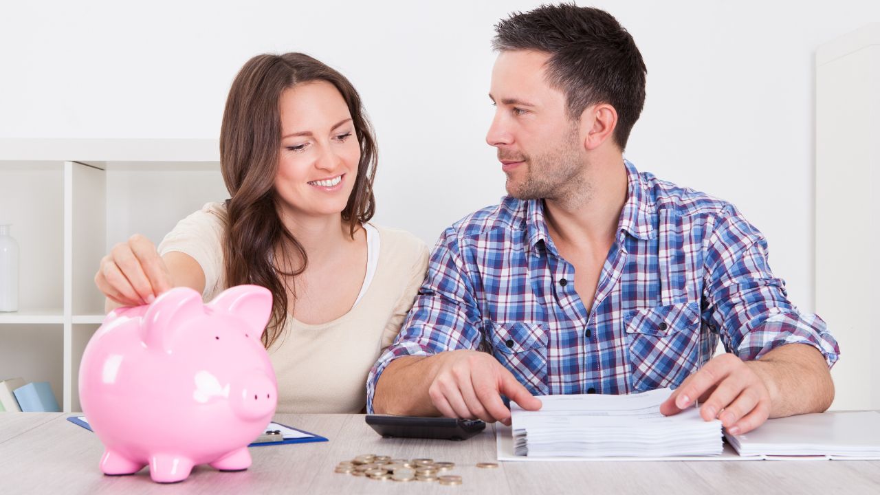 man and woman making a budget, pink piggy bank beside the woman and coins on the table