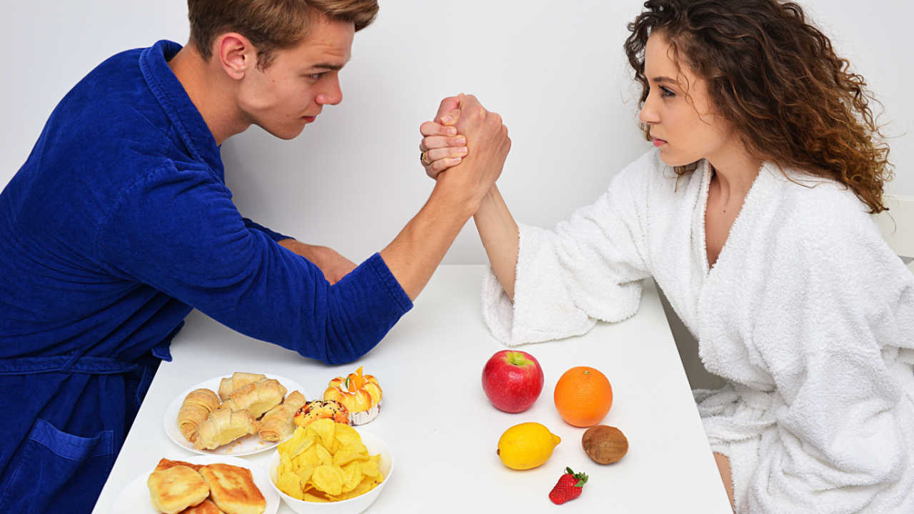 man and woman arm wrestling over breakfast table
