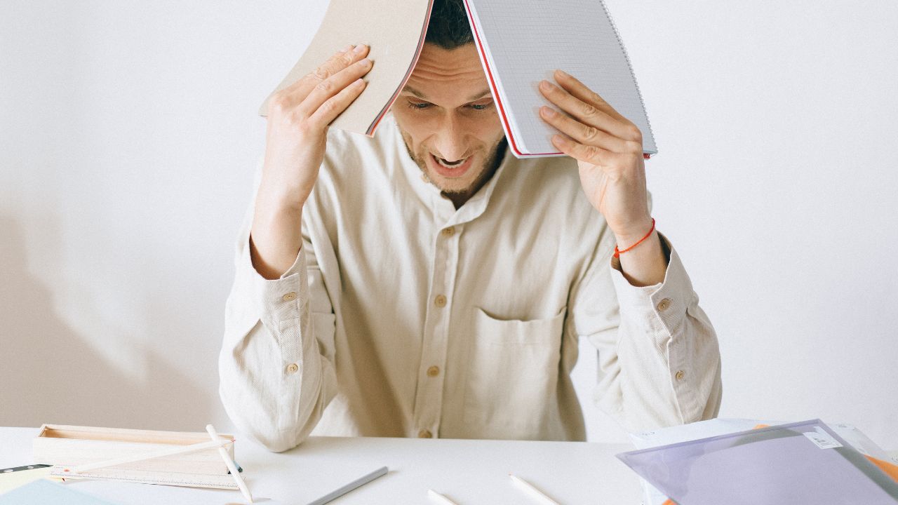 Man feeling overworked, has notebooks on head