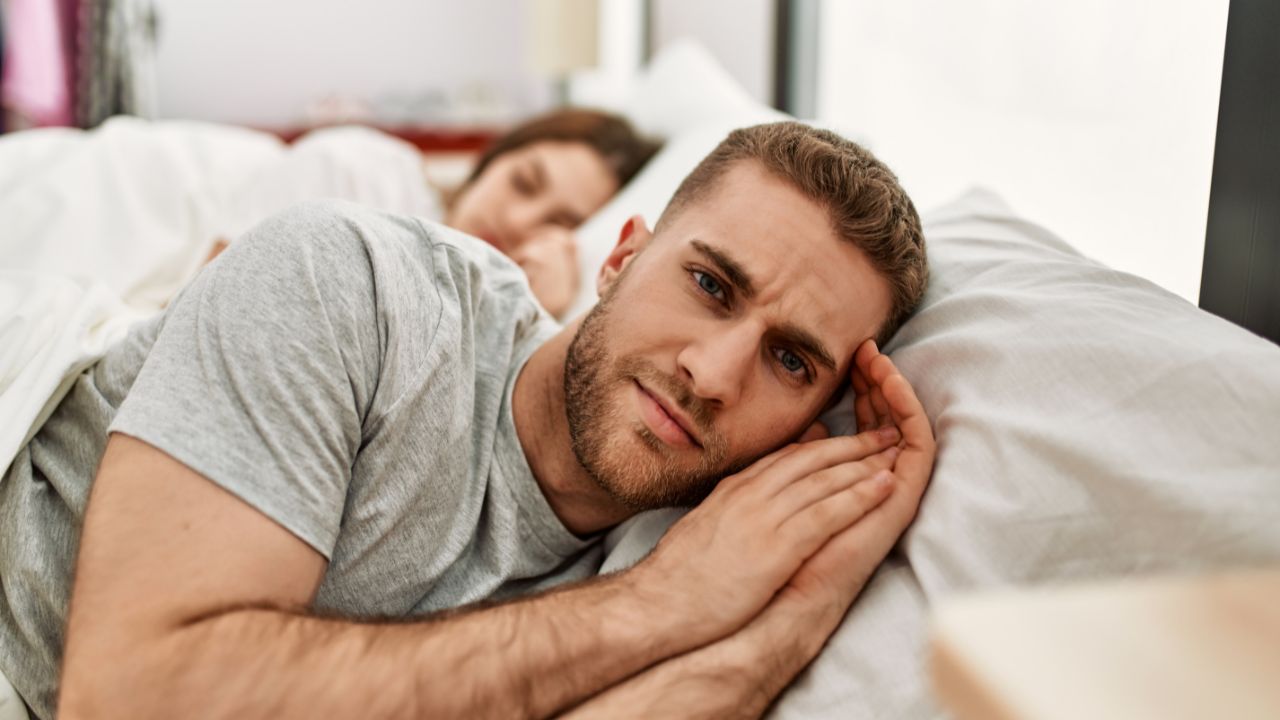 man sleeping at edge of bed with woman