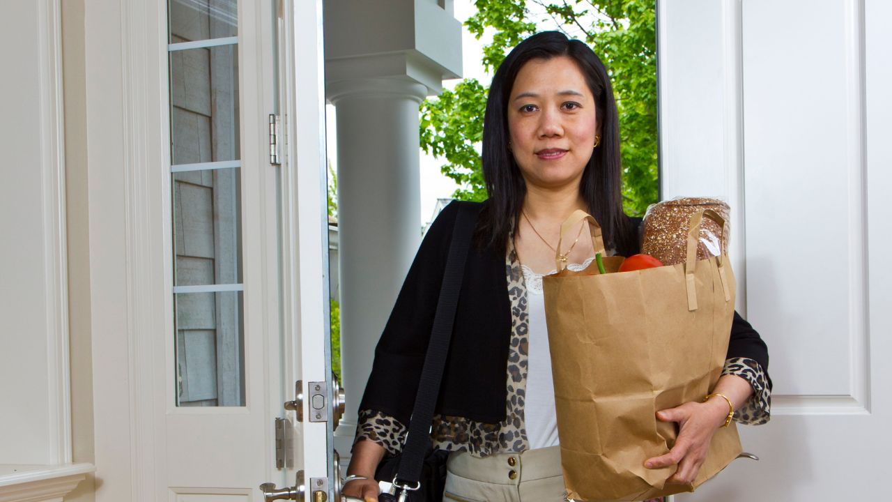 woman walking through the door coming into the house carrying a grocery bag