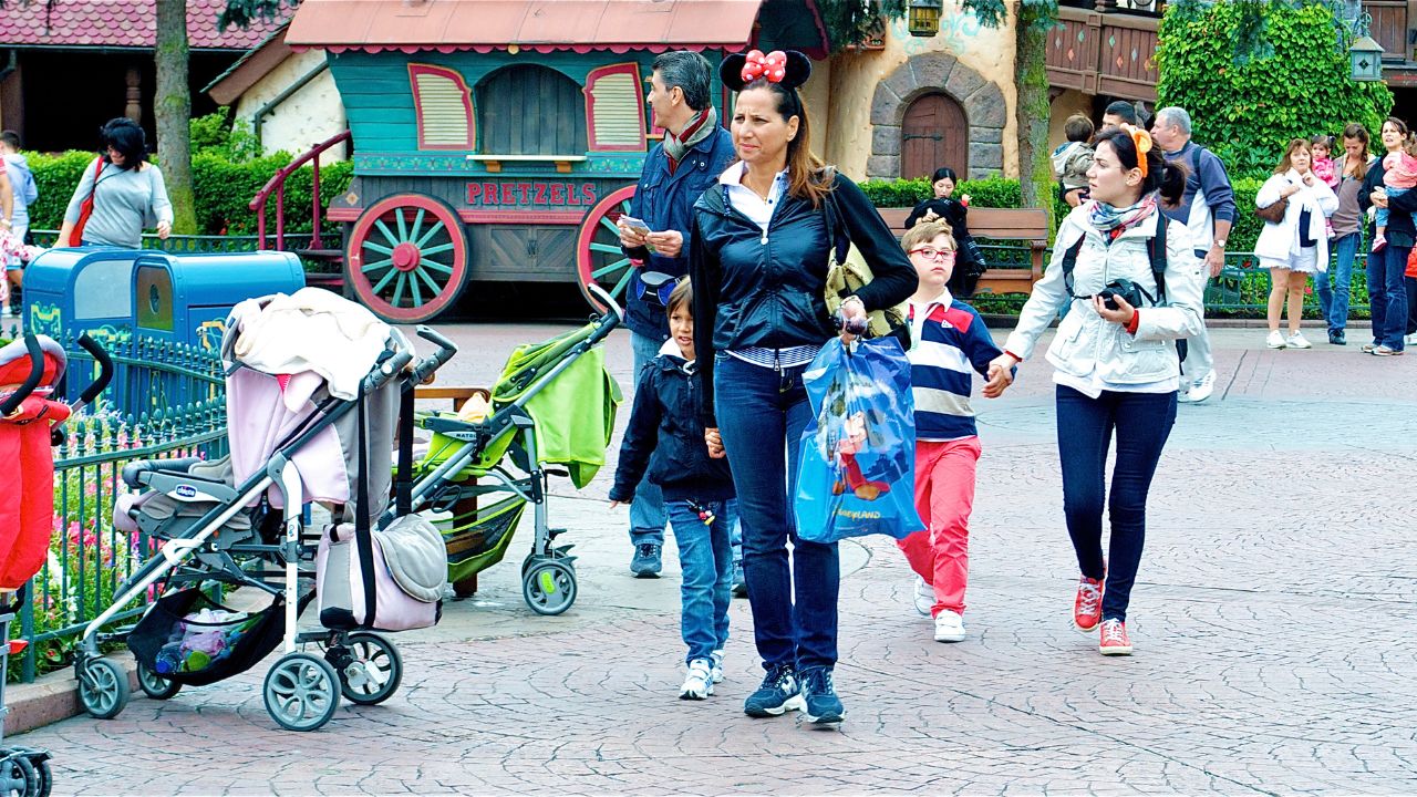 mother wearing minnie ears, holding son's hand. Other families walking in the back at Disney World