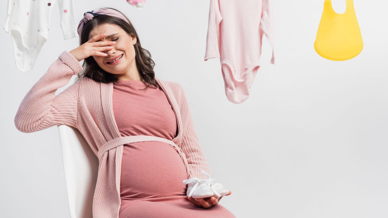 pregnant woman dressed in pink sitting on chair and crying