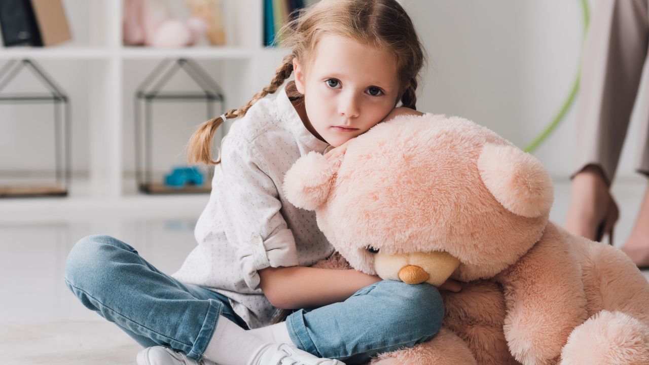 little girl with pink teddy bear looking sad