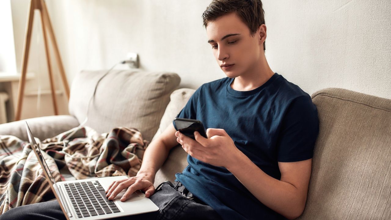 teenage boy sitting on couch with laptop and phone