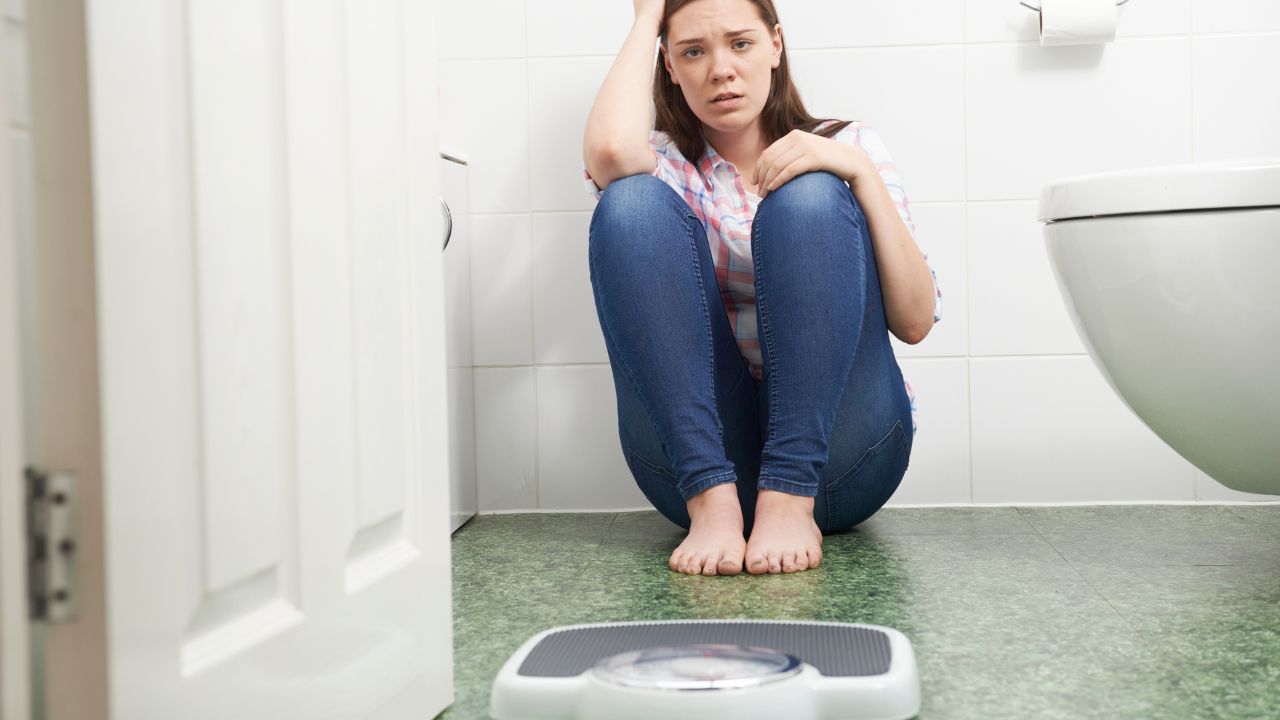 teenage girl sitting on the bathroom floor upset, looking at a scale