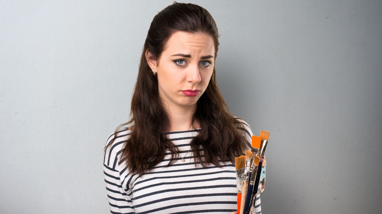 woman artist looking sad and holding paint brushes
