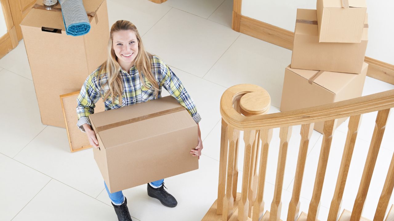 woman carrying a moving box and standing by the stair railing