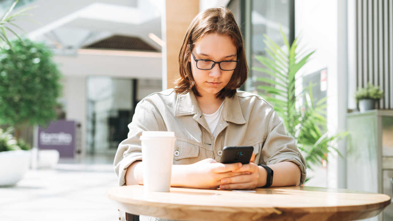 woman sitting at cafe with coffee, using phone, sending a text message