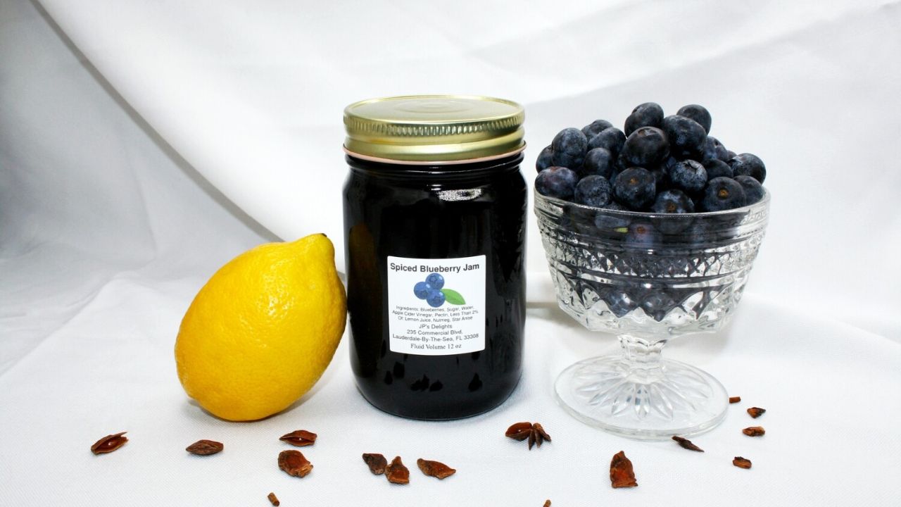 jar of spiced blueberry jam beside a lemon and a bowl of blueberries